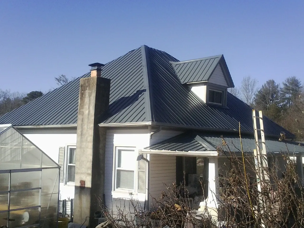 Dark blue standing seam metal roof on a white farmhouse with dormer — Slate & Tile Roof Repair by Roofing Brothers in Alamance