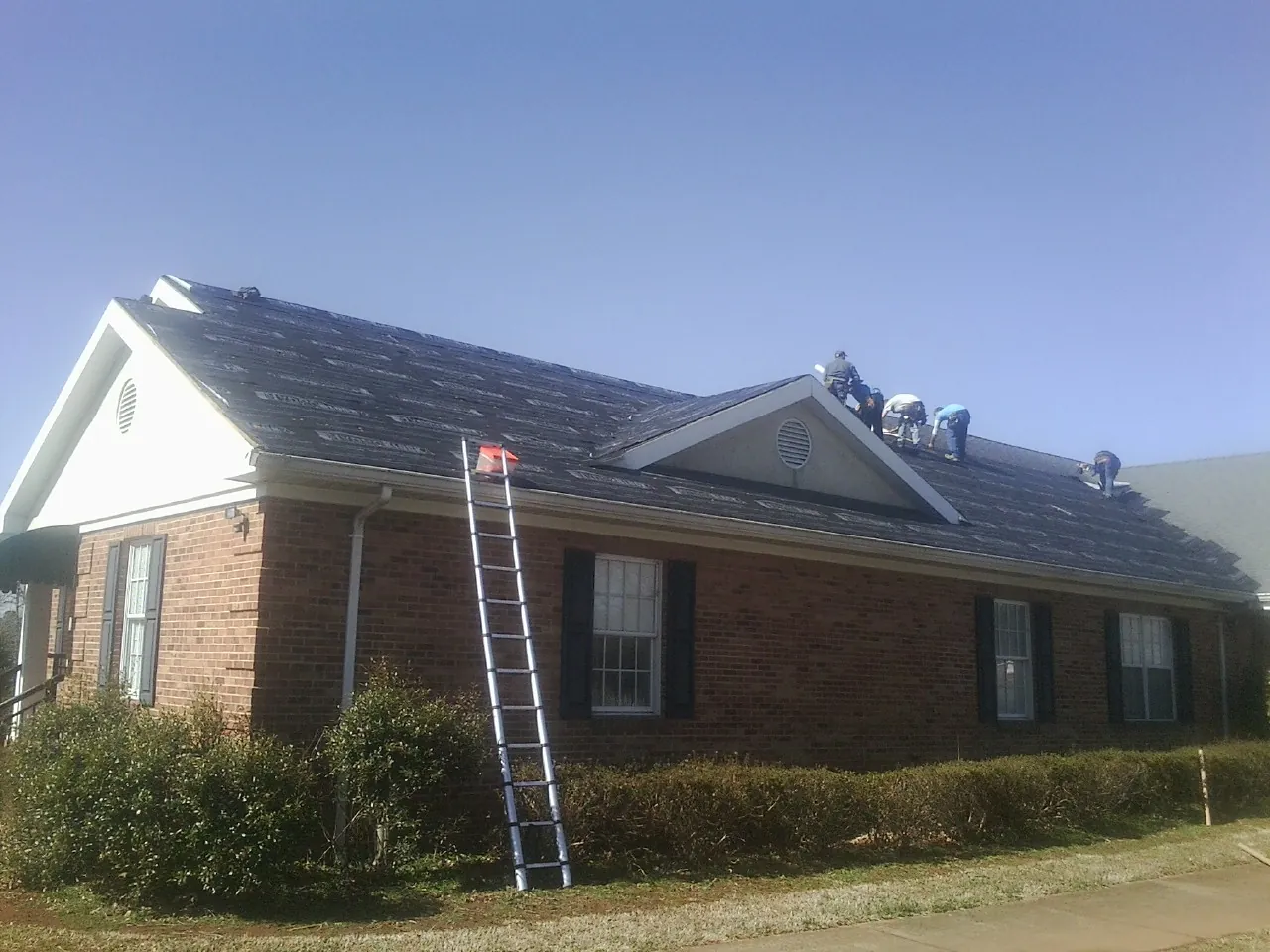 Crew tearing shingles off a brick ranch roof with a ladder set — Metal Roof Repair work by our crew in Alamance