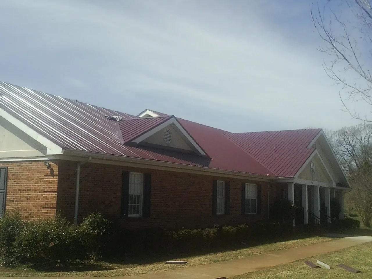 Red metal roof with gabled entries on a long brick building, from a Hail Damage Roof Repair job in Alamance