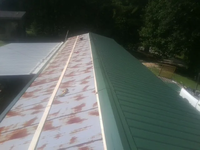Old rusted panels beside newly installed green metal roofing — Wind Damage Roof Repair by Roofing Brothers in Alamance