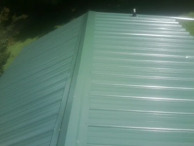 New green metal panels meeting at the ridge of a roof — Flat Roof Repair work by our crew in Alamance