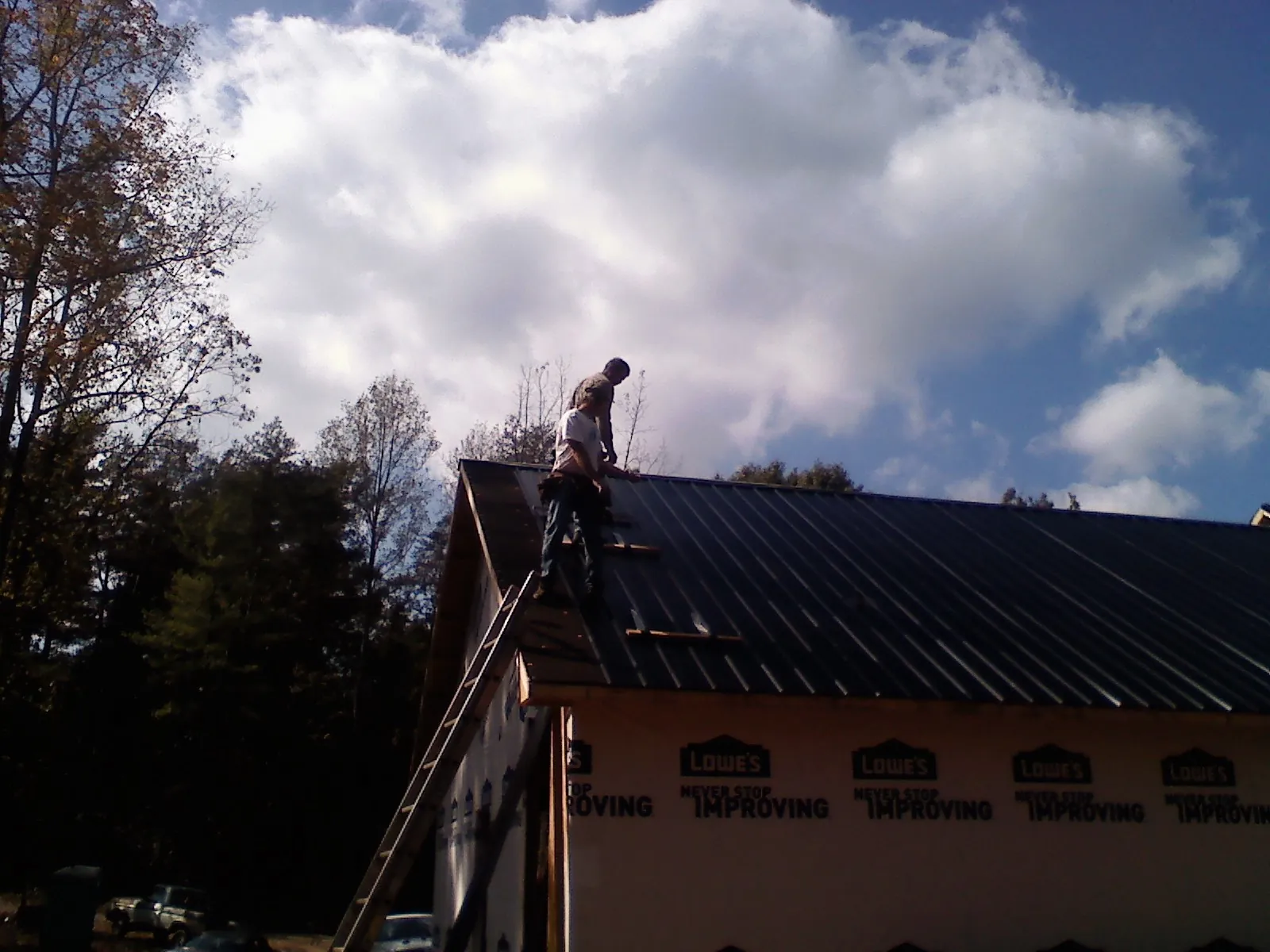 Roofer fastening dark metal panels high against a cloudy sky, from a Roof Inspection job in Alamance