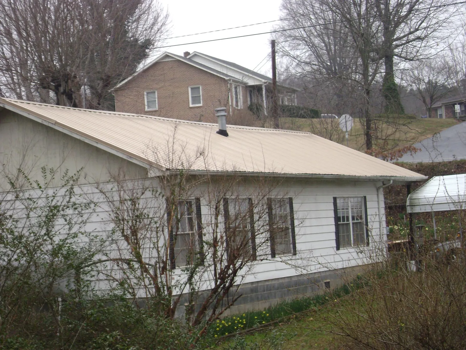 Tan metal roof on a white sided house set into a hillside — Commercial Roofing by Roofing Brothers in Alamance