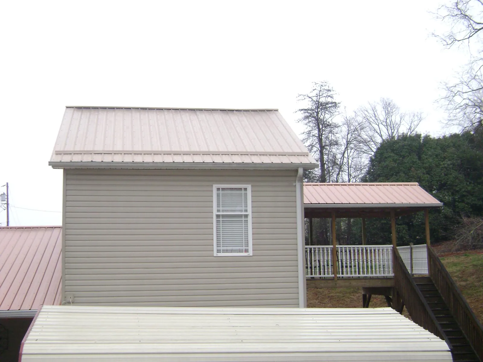 Tan metal roofs on a two story addition and attached porch, from a Roof Replacement job in Alamance